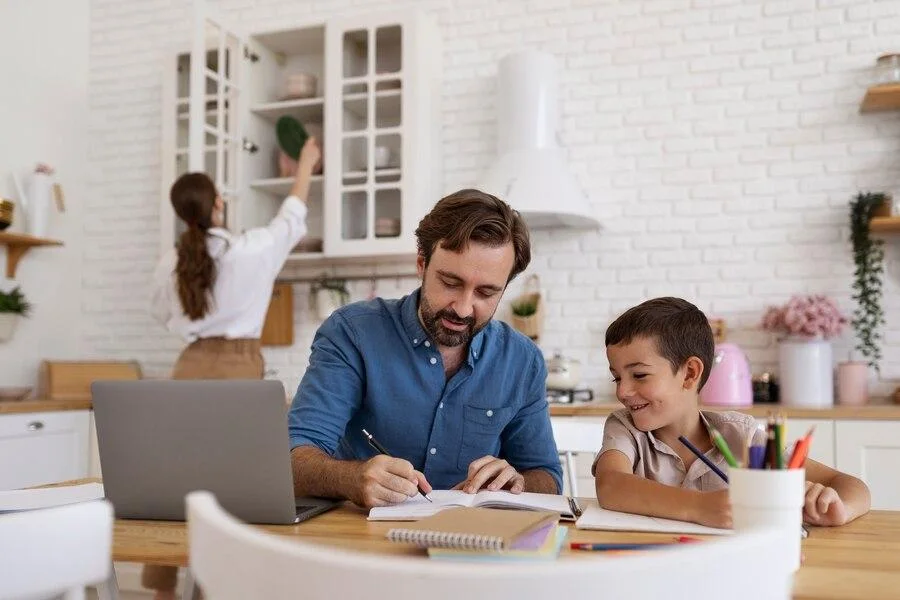 Father teaching son at the kitchen table while mother puts away dishes