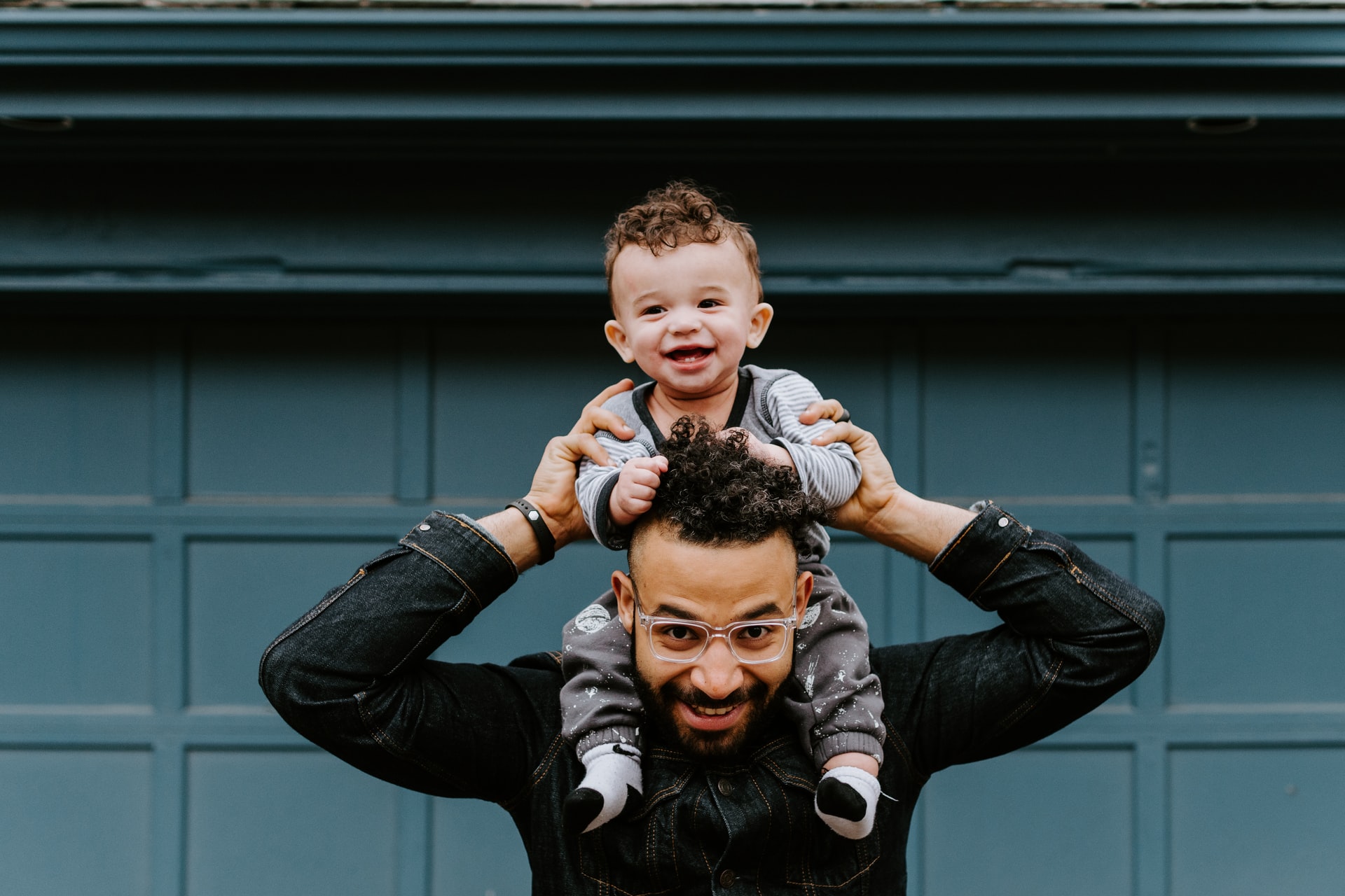 A smiling child sitting on an adult’s shoulders