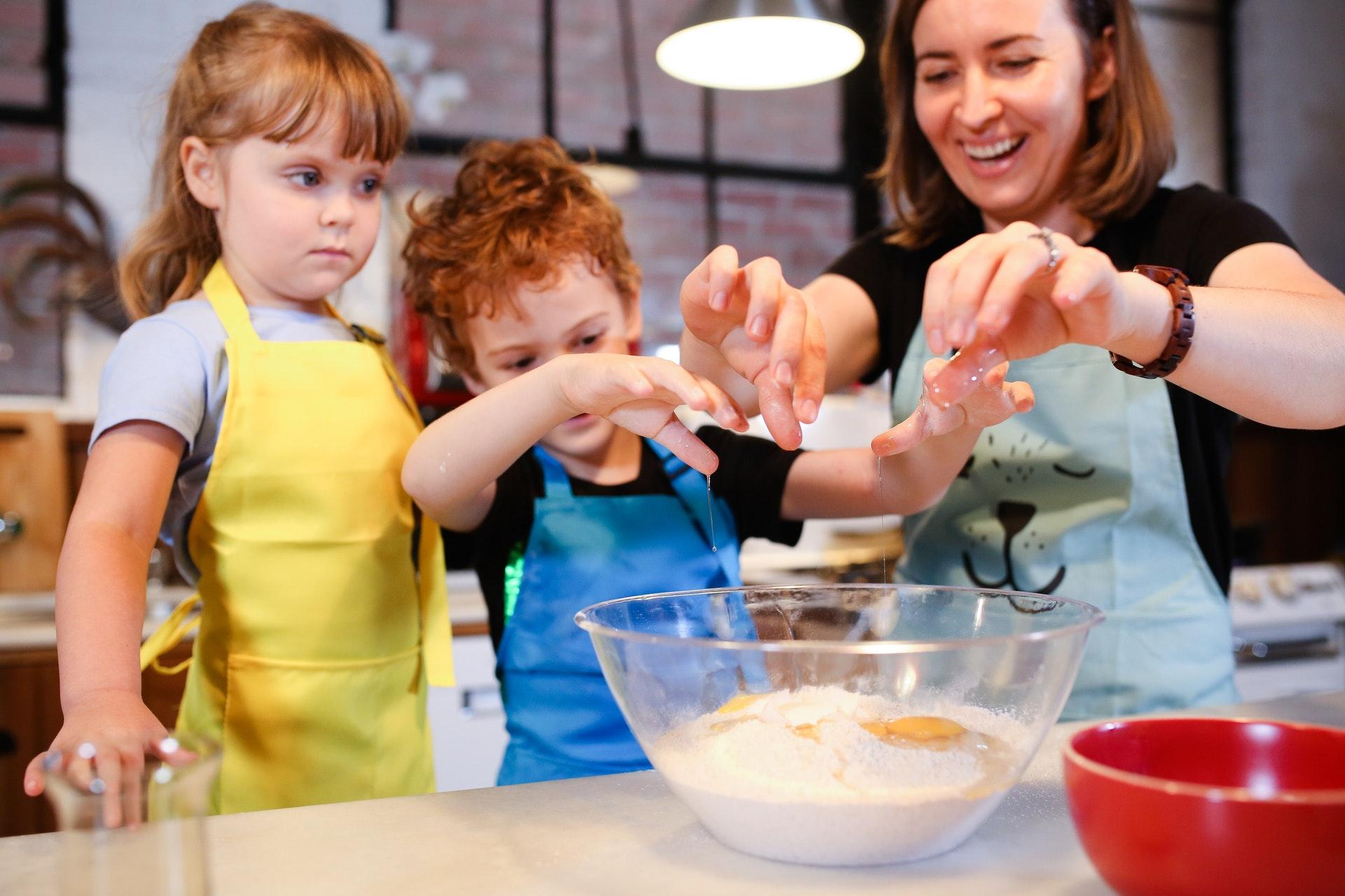 An adult helps children stir ingredients in a mixing bowl